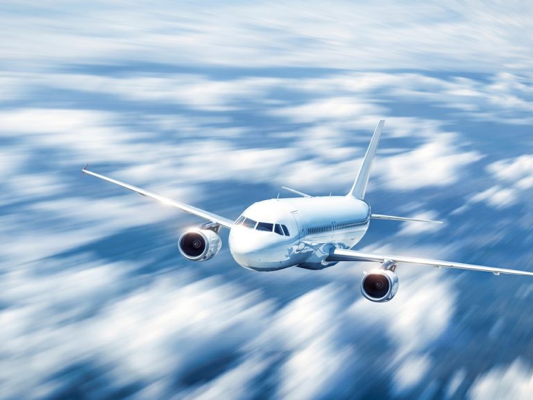Aerospace industry: a twin-engine commercial airliner with a plain white unbranded fuselage flying above a sea of sunlit clouds