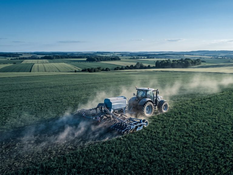 Agriculture industry: a large modern tractor pulling a wide seed drill across a vast green field at golden hour
