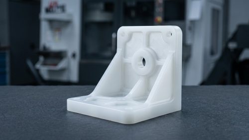 CNC machined polypropylene bracket part on dark workshop table
