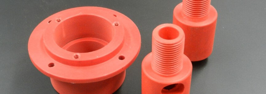 Three red plastic machined parts on dark surface