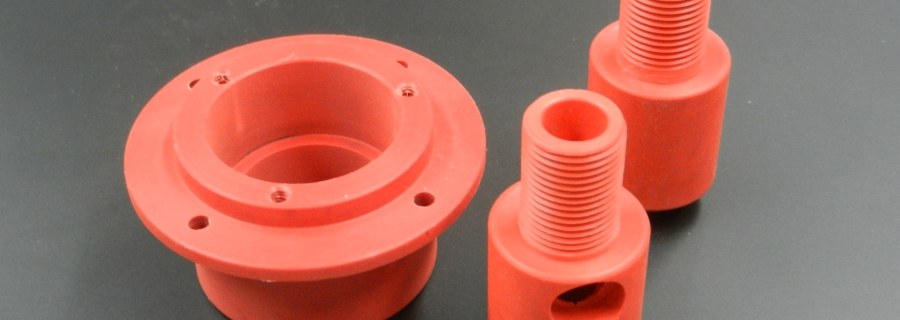 Three red machined plastic parts on dark surface