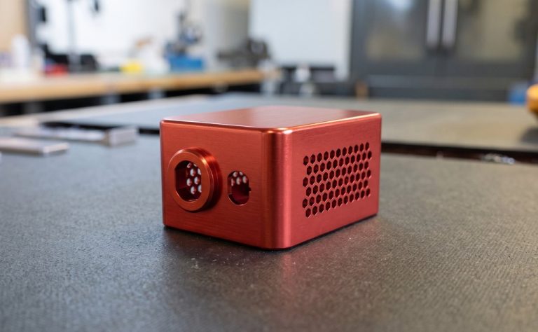 Red anodized aluminum housing with honeycomb vent held in gloved hands