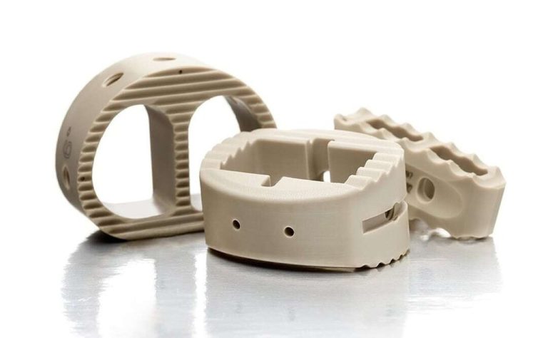 Three beige machined PEEK parts on reflective surface