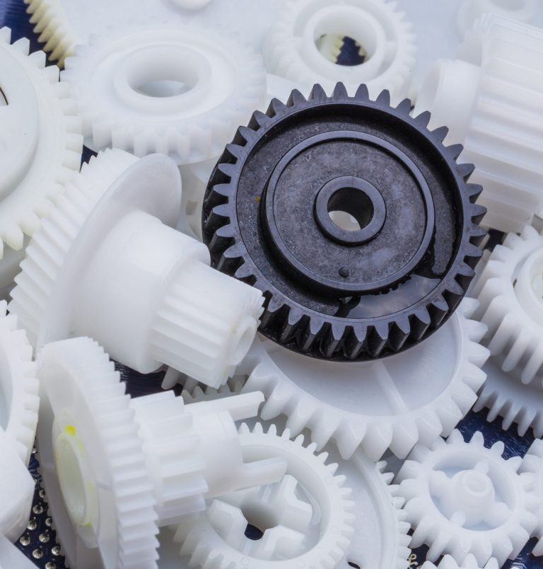Delrin plastic gears, one black, scattered on blue