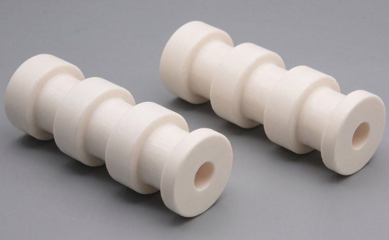 Two white ceramic machined parts with stepped cylindrical shapes
