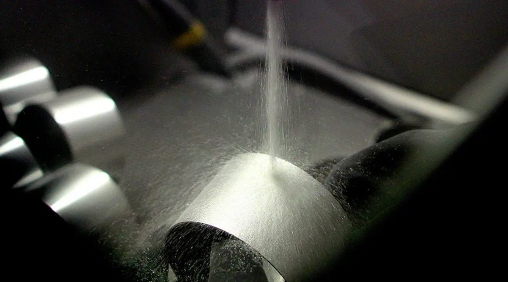 Media blasting nozzle spraying machined aluminum bracket surface
