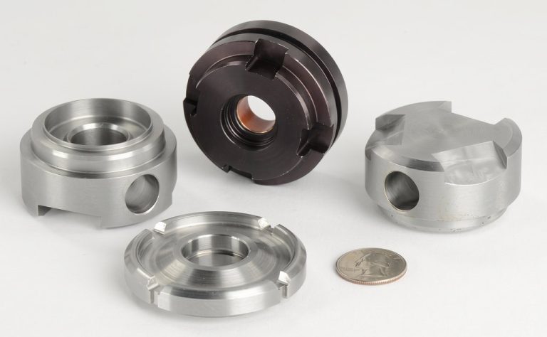 Four precision machined metal parts with coin for scale