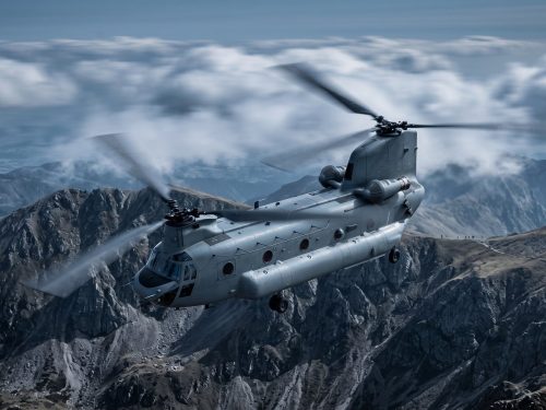 Military & Defense industry: a grey military transport helicopter flying low over rugged mountains at dusk