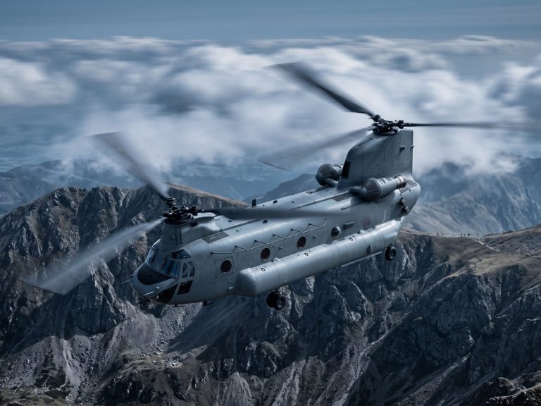 Military & Defense industry: a grey military transport helicopter flying low over rugged mountains at dusk