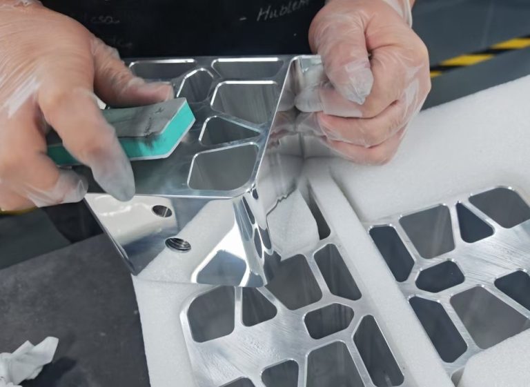 Worker wrapping machined aluminum bracket part in foam packaging