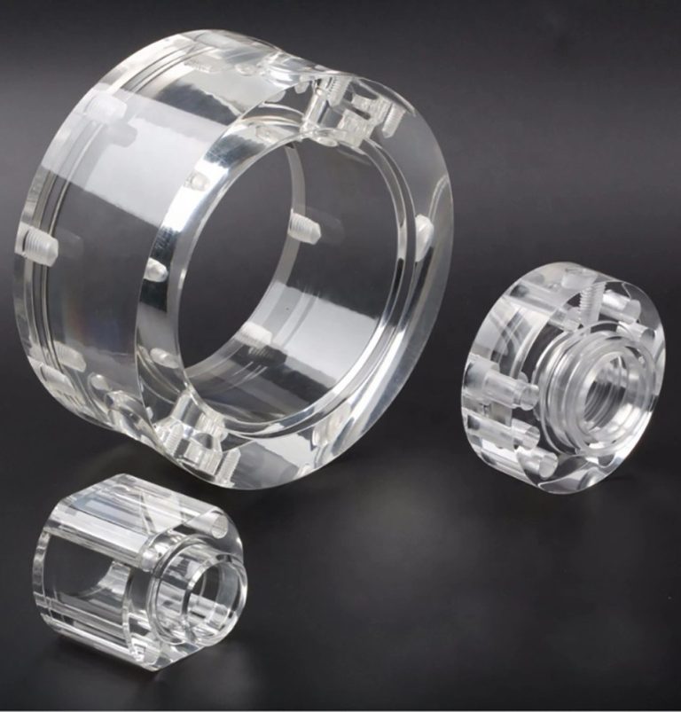Three clear machined acrylic parts on dark surface