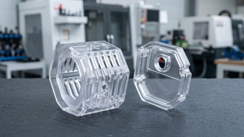 Two clear polished polycarbonate machined parts on dark surface