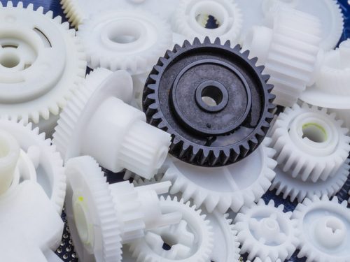 Delrin plastic gears, one black, scattered on blue