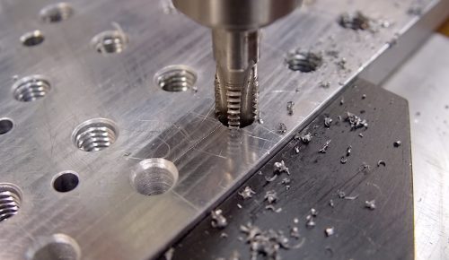 CNC tapping head cutting internal threads into stainless steel block