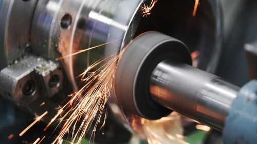 Cylindrical grinding machine shaping a steel shaft with sparks flying